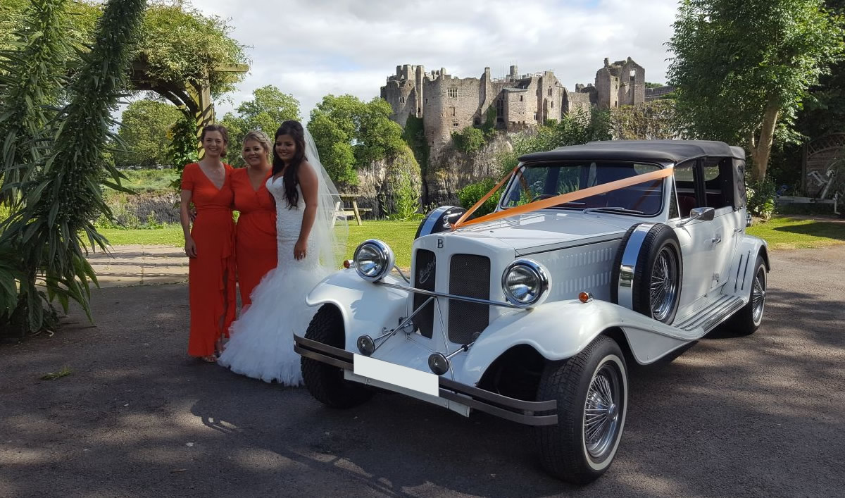 Bride and bridesmaids stand next to wedding car at Chepstow castle
