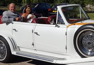Bride and groom sit in wedding car with roof down