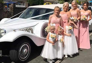 Bridesmaids pose with wedding car